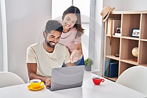 Man and woman couple sitting on table drinking coffee using laptop at home