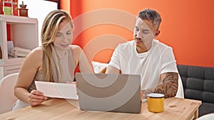 Man and woman couple using laptop reading document at dinning room