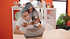 Man and woman couple using laptop sitting on table kissing at dinning room