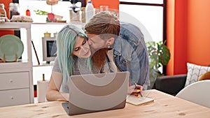 Man and woman couple using laptop writing notebook at dinning room