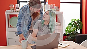 Man and woman couple using laptop writing notebook holding cup of coffee at dinning room