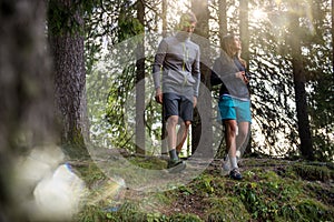 Man and woman couple walking in forest woods with sun flare light. Group of friends people summer adventure journey in