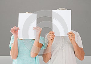 Man and woman covering their face behind paper against grey background