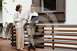 Man and woman discussing business details and using laptop while standing outdoors