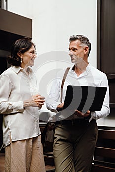 Man and woman discussing business details and using laptop while standing outdoors