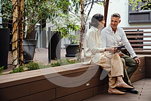 Man and woman discussing business details and using tablet while sitting outdoors