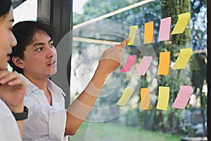 man & woman discussing creative idea with adhesive notes on glass wall at workplace. Sticky note paper reminder schedule