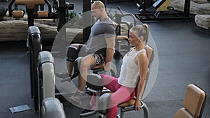 Man and woman doing exercise in machine in gym.