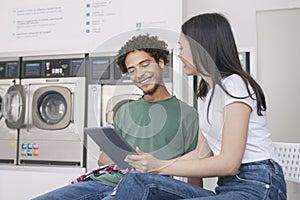 Man And Woman Doing Laundry Using Digital Tablet At Laundromat