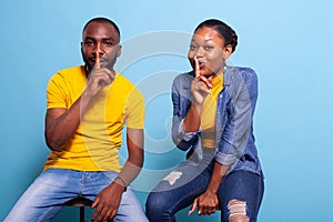 Man and woman doing secret sign with finger over mouth