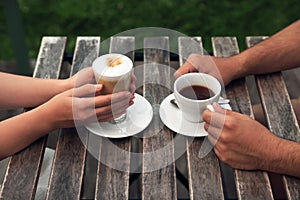 Man and woman drinking coffee at wooden table in outdoor cafe, closeup