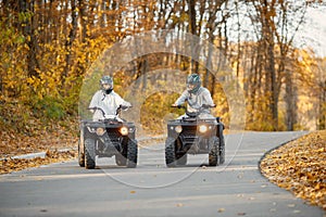 Man and woman driving quad bikes in autumn forest