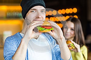 Man and woman eating burger. Young girl and young man are holding burgers on hands