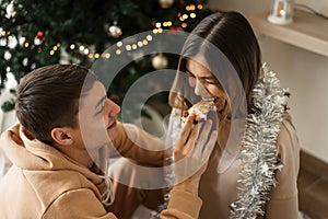 Man and woman eating pizza at home near Christmas tree and having fun