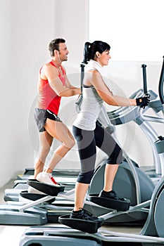 Man and woman with elliptical cross trainer at gym