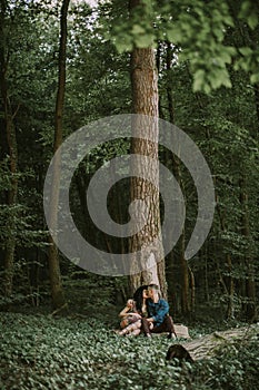 man and woman, enjoying walk in the forest, sitting under the big tree, hugging and kissing