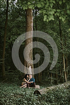 man and woman, enjoying walk in the forest, sitting under the big tree, hugging and kissing