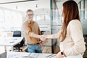 A man and woman exchange a firm handshake in a bright office