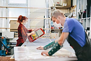 Man and woman in face masks working on glass pane in glazier workshop