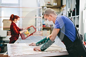 Man and woman in face masks working on glass pane in glazier workshop