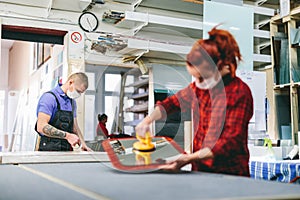 Man and woman in face masks working on glass pane in glazier workshop