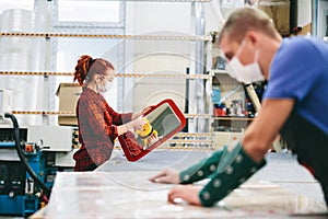 Man and woman in face masks working on glass pane in glazier workshop