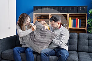 Man and woman fighting with cushion sitting on sofa with dog at home