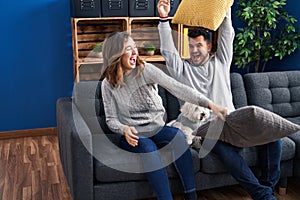 Man and woman fighting with cushion sitting on sofa with dog at home