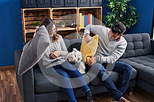 Man and woman fighting with cushion sitting on sofa with dog at home