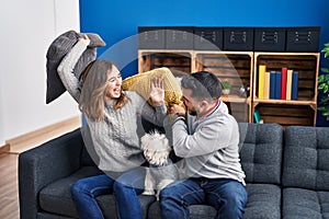 Man and woman fighting with cushion sitting on sofa with dog at home