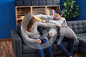 Man and woman fighting with cushion sitting on sofa with dog at home