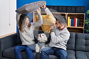 Man and woman fighting with cushion sitting on sofa with dog at home