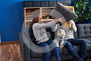 Man and woman fighting with cushion sitting on sofa with dog at home