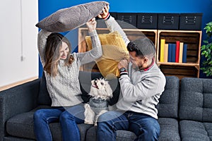 Man and woman fighting with cushion sitting on sofa with dog at home