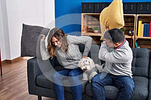 Man and woman fighting with cushion sitting on sofa with dog at home