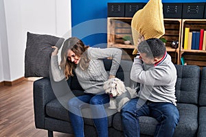 Man and woman fighting with cushion sitting on sofa with dog at home