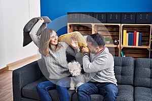 Man and woman fighting with cushion sitting on sofa with dog at home