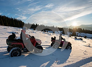 Man and woman on four-wheelers ATV bikes on snow, enjoying sunset in the the mountains in winter