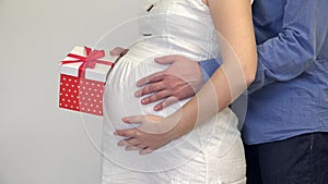 Man and woman hands caressing pregnant wife belly husband holding a present box