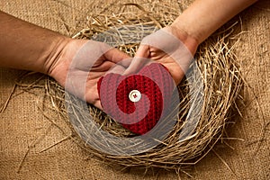 Man and woman hands holding decorative red heart in nest