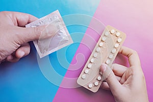 Man and woman hands are hording contraception pills and condom on blue and pink background.