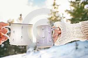 Man and woman hands in knitting mittens taking cups of hot drink