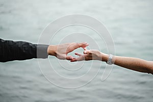 Man and woman hands reaching out, holding, near water