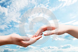 Man and woman hands touch in gentle, soft way on blue sunny sky