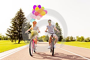 Man and woman having fun on summer day and cycling with balloons