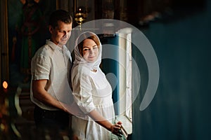 man and woman in headscarf and light-colored robes by window in church.