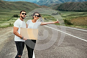 A man and a woman are hitchhiking. Wanderlust, autostop journey concept. Young people traveling hitchhiking. Hitchhiking couple