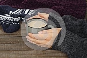 Closeup of woman hands who holding a cup of hot chocolate, knitted scarf and mittens on the wooden rustic table