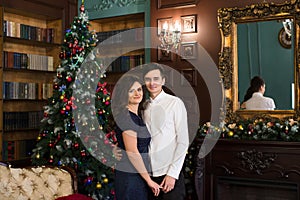 Man and woman holding hands near Christmas tree and fireplace in the Christmas atmosphere