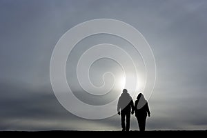 Man and woman holding hands and walking together towards rising sun